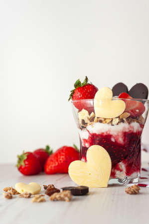 Strawberry valentines day dessert decorated with heart-shaped chocolate and ripe berries vertical photo Two glasses with a sweet breakfast of cream cheese and pureed berries on a white wooden tableの写真素材