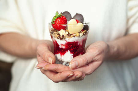 Womens hands with a glass of sweet creamy dessert on st. Valentines Day. dessert decorated with strawberries and chocolate in the shape of a heartの写真素材
