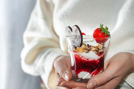 Womens hands with a glass of sweet creamy dessert on st. Valentines Day. dessert decorated with strawberries and chocolate in the shape of a heartの写真素材