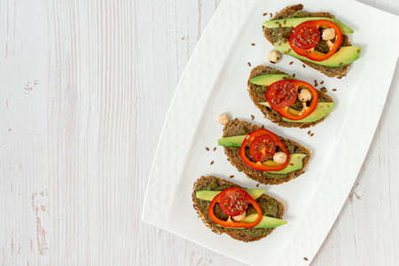 Rye bread sandwiches with vegetables and spicy sauce on a white plate and wooden table. Vegan, healthy nutrition. Diet breakfast. Top view, space for text.の写真素材