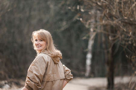 A beautiful happy middle-aged blonde woman in a beige jacket walks through a sunny spring or winter park. The woman looks around and laughs. Happiness and mental health.の写真素材
