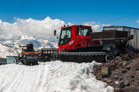 Red snowcat transport on white snow cleans ski track near mountain shelter. Caucasus Mountainの写真素材