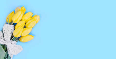 Yellow Tulip Bouquet with White Ribbon on Blue Background, copy space, flat layの写真素材