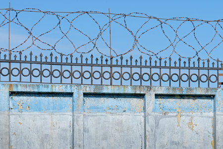 Old stone cement fence wall with iron grating and barbed wire on top, security