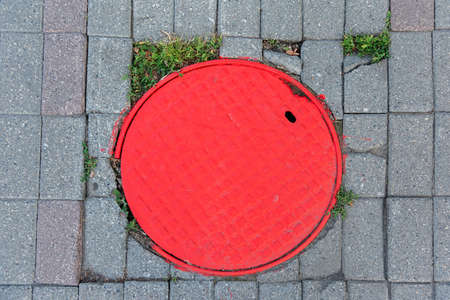 Round red metal sewer manhole cover on the sidewalkの写真素材