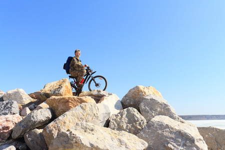 The man with bicycle costs on stones at the river which has been held down by iceの写真素材