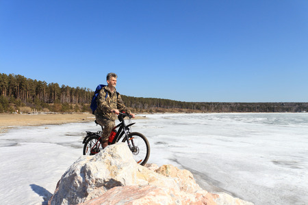 The man with bicycle costs on stones at the river which has been held down by iceの写真素材