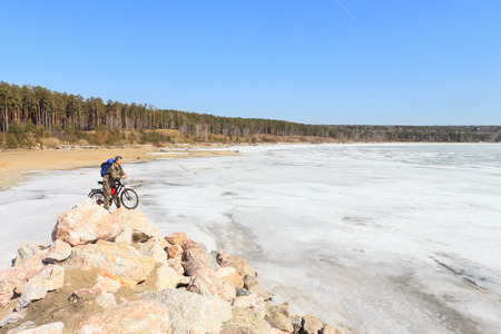 The man with bicycle costs on stones at the river which has been held down by iceの写真素材