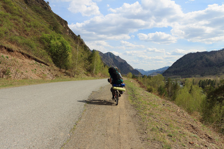 The man with a backpack goes by bicycle on the road among mountainsの写真素材