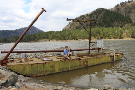 The man works at water pump station on the barge among mountainsの写真素材
