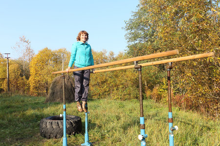 The woman hangs on bars on is sports to a platform among the autumn wood