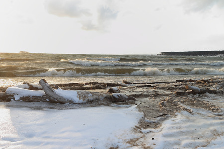 The running waves on the sandy snow-covered coast on the river against the skyの写真素材