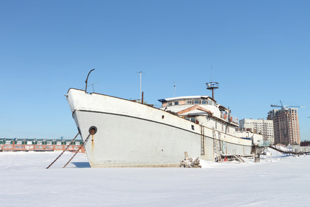 Decommissioned river vessel standing on the river which is held down by ice in harbor in the winterの写真素材
