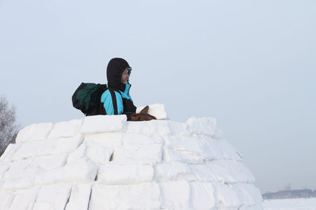 The man with a backpack on a snow field building of pieces of snow an igloo in the winter