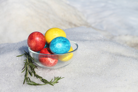 Multicolored Easter eggs in the glass plate standing on snow outdoorsの写真素材