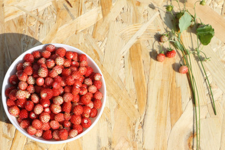 Ripe red wild strawberry in a plate on a wooden table outdoors