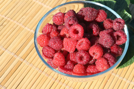 Glass plate with fresh ripe raspberry standing on a table in a garden