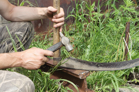 The man beats off scythe a hammer in a gardenの写真素材