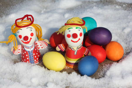 Color Easter eggs with a toy figure of the little man on a napkin in snow outdoorsの写真素材