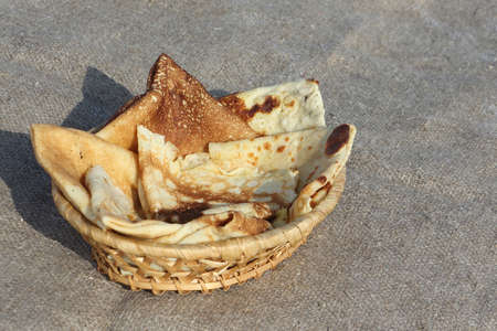 Baked pancakes in a wooden basket on a brown napkin against snow outdoorsの写真素材