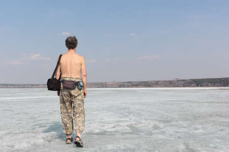 The gray-haired man with a bare torso going on ice of the thawing river in the springの写真素材