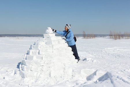 Woman in a blue jacket building an igloo on a snow glade in the winter