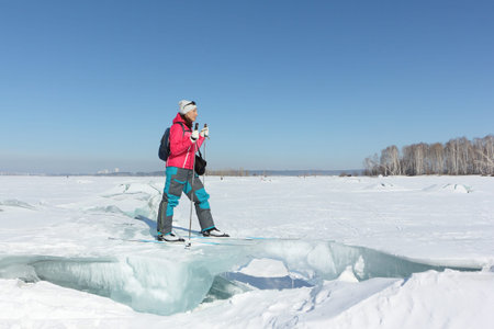 Happy woman skier in a red jacket standing on an ice floe on a frozen river, Ob reservoir, Russiaの写真素材