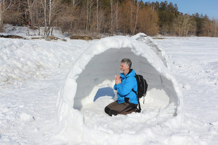 Man resting in unfinished an igloo on a glade in the winter