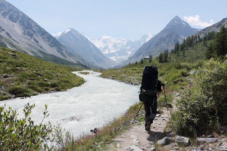 Man with a backpack walking along the path along the Akkem River, against the background of the Belukha Mountain, Altai, Russiaの写真素材