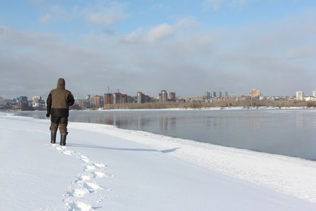 Tall man in warm clothes walking along the snowy bank of a frozen river, Ob River, Russiaの写真素材