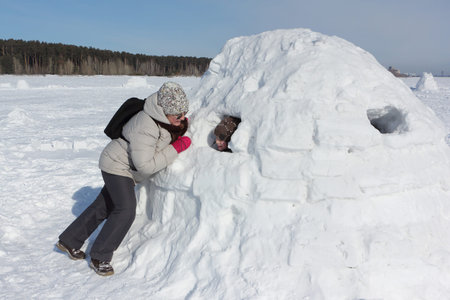 Woman in a light jacket talking to a boy sitting in an igloo