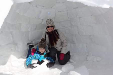 Happy grandmother and grandson sitting in an igloo on a snowy glade in winter, Novosibirsk, Russia
