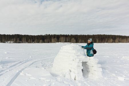 Happy woman in warm clothes building an igloo on a snow glade in the winter,  Novosibirsk, Russiaの写真素材