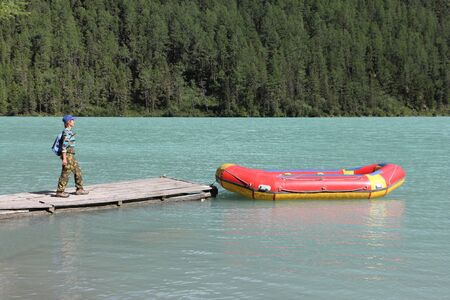 Happy woman with backpack walking on the pier to the red boat, Kucherlinsky Lake, Belukha Natural Park, Altai Mountains, Russiaの写真素材