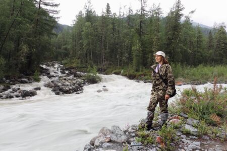 Happy woman standing on the shore of a mountain river. The confluence of the Tekelu River into the Akkem River, Altai Mountains, Russiaの写真素材