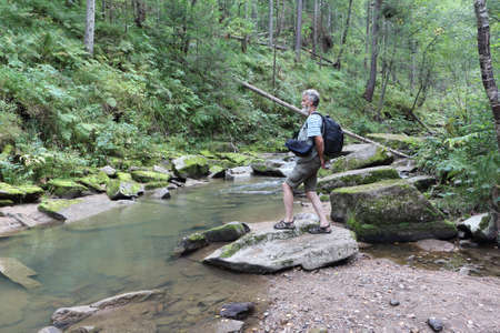 Man with a backpack sitting on a stone near a mountain river on a summer day, Belokurikha River, Belokurikha City, Altai Mountainsの写真素材