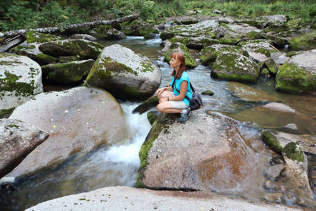 Happy woman with red hair standing on a stone by the river in summer, Belokurikha River, Belokurikha City, Altai Mountains, Russiaの写真素材
