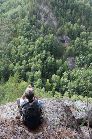 Man photographing with his phone at the edge of a cliff, Altai Mountains, Belokurikha 2, Russiaの写真素材