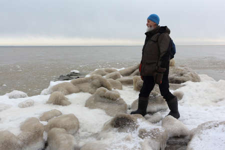 Man with a backpack standing in the evening on the ice near a freezing river in autumn, Ob reservoir, Novosibirsk city, Russiaの写真素材