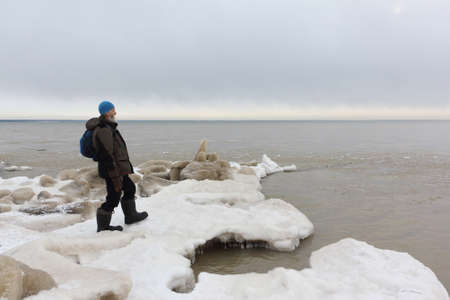 Man with a backpack standing in the evening on the ice near a freezing river in autumn, Ob reservoir, Novosibirsk city, Russiaの写真素材