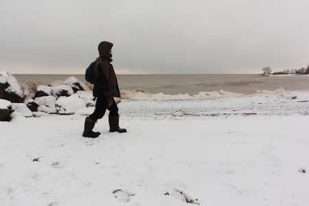 Man with a backpack walking in the evening along the bank of a freezing river in autumn, Ob reservoir, Novosibirsk city, Russiaの写真素材