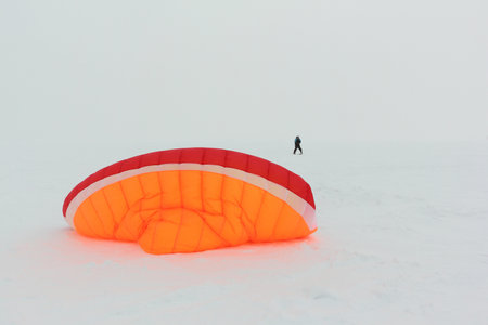 Man training with a kite in a snowstorm on a frozen river in winter, Ob reservoir, Novosibirsk, Russiaの写真素材