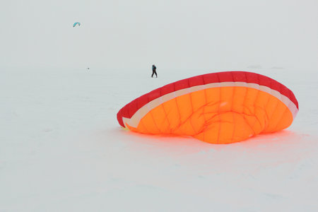 Man training with a kite in a snowstorm on a frozen river in winter, Ob reservoir, Novosibirsk, Russiaの写真素材