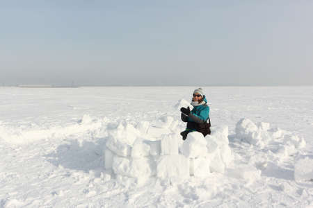 Happy woman in a green jacket building an igloo on the snow in winter, Ob reservoir, Novosibirsk, Russiaの写真素材