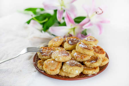 breakfast with cheesecakes sprinkled with powdered sugar and pink lilies on a white table lit by the sun, horizontal,の写真素材