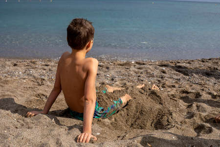 happy boy sits on a sandy beach near the sea and looks into the distance, vacationの写真素材