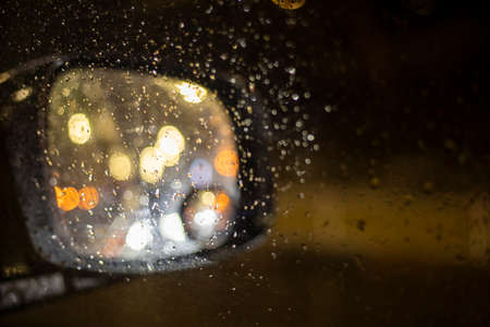 abstract blurred background on the right side mirror of a car with bright lights during a traffic jam in the rainの写真素材