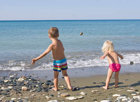 happy boy and girl throwing pebbles on the beach into the water, having a family vacationの写真素材