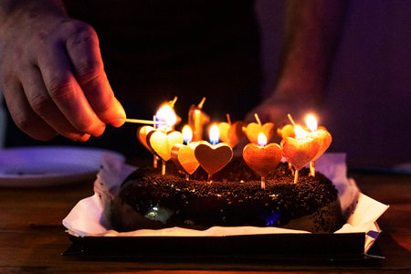 man's hand lights candles on a birthday cake with hearts. holiday partyの写真素材