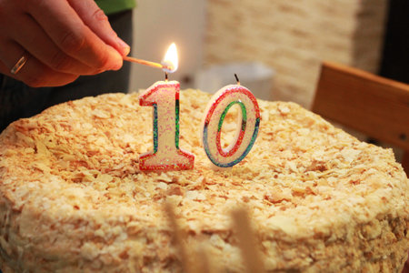 man's hand set fire to birthday candles on a cake with the number 10の写真素材